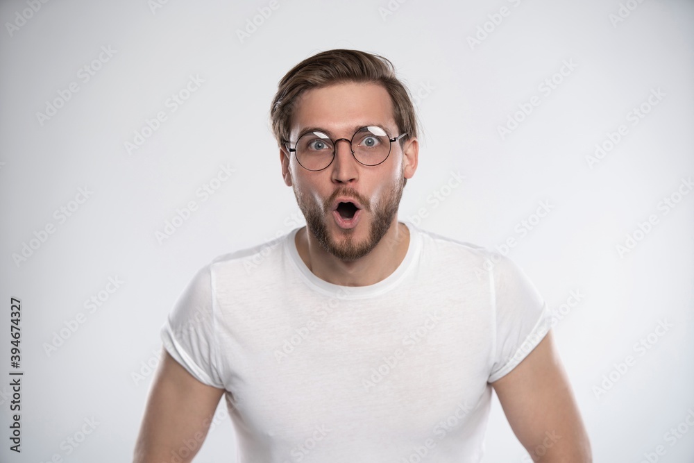 Attractive young bearded man looks with astonishment into camera, being amazed with news. Facial expression Attractive young bearded man looks with astonishment into camera, being amazed with news. Facial expression