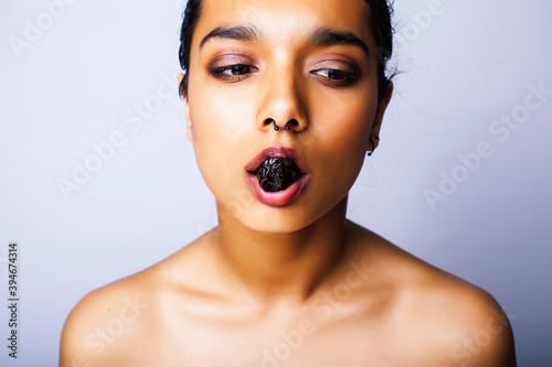 young pretty indian woman with dry fruit in mouth on white background