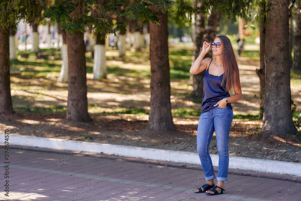 Pretty woman stands on the path among the old pine trees of the city park. Copy space. Pretty woman stands on the path among the old pine trees of the city park. Copy space.