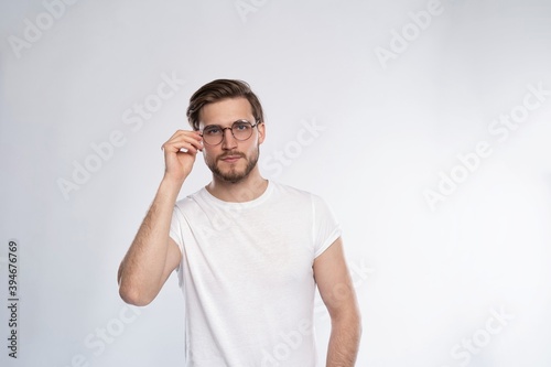 Portrait of a smart young man in glasses standing against white background. © opolja