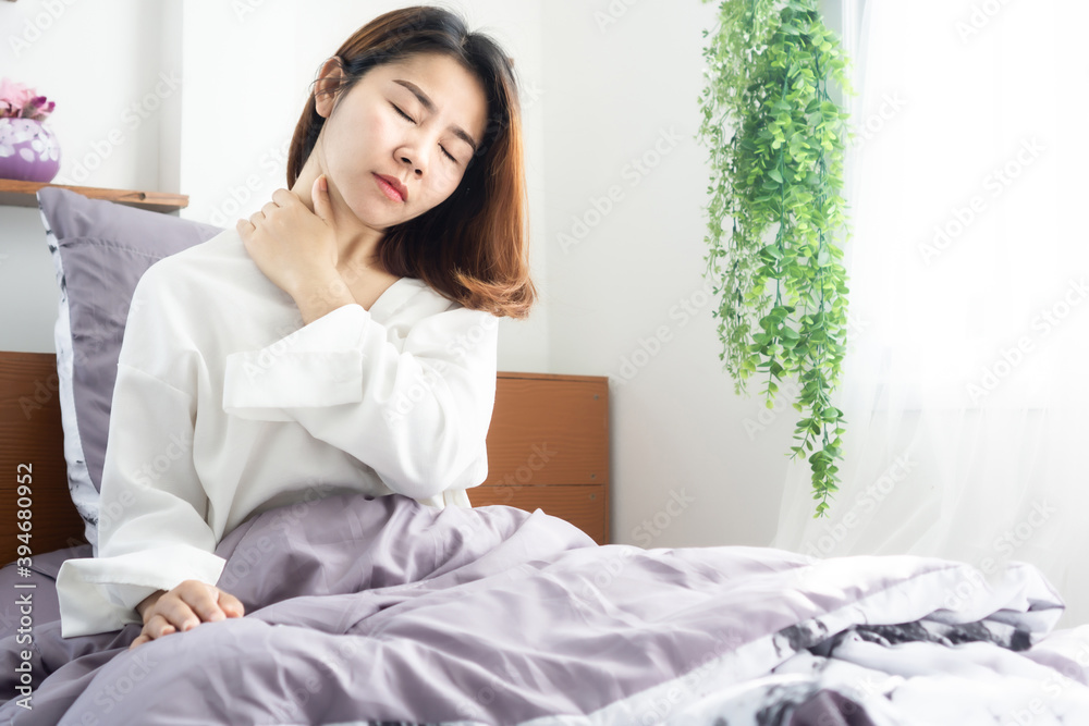 Asian woman waking up in bed and suffering from neck pain using hand messaging her neck muscle Asian woman waking up in bed and suffering from neck pain using hand messaging her neck muscle