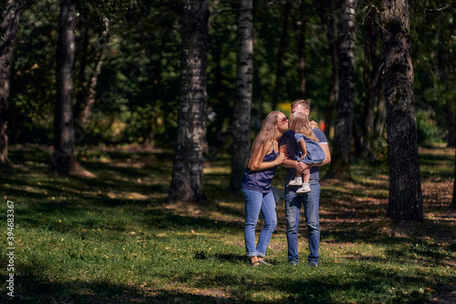 Mom kisses her daughter sitting in her father's arms. The family is resting in nature. Summer sunny day. Copy space. © Aleksandr