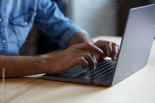 Close-up photo of male hands with laptop. Freelancer sitting on his workplace, texting message, searching web, browsing information using laptop keyboard. Online education, remote working.