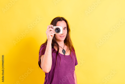 Pretty young girl takes photos with an evil camera, isolated on yellow studio background. © Joaquin Corbalan