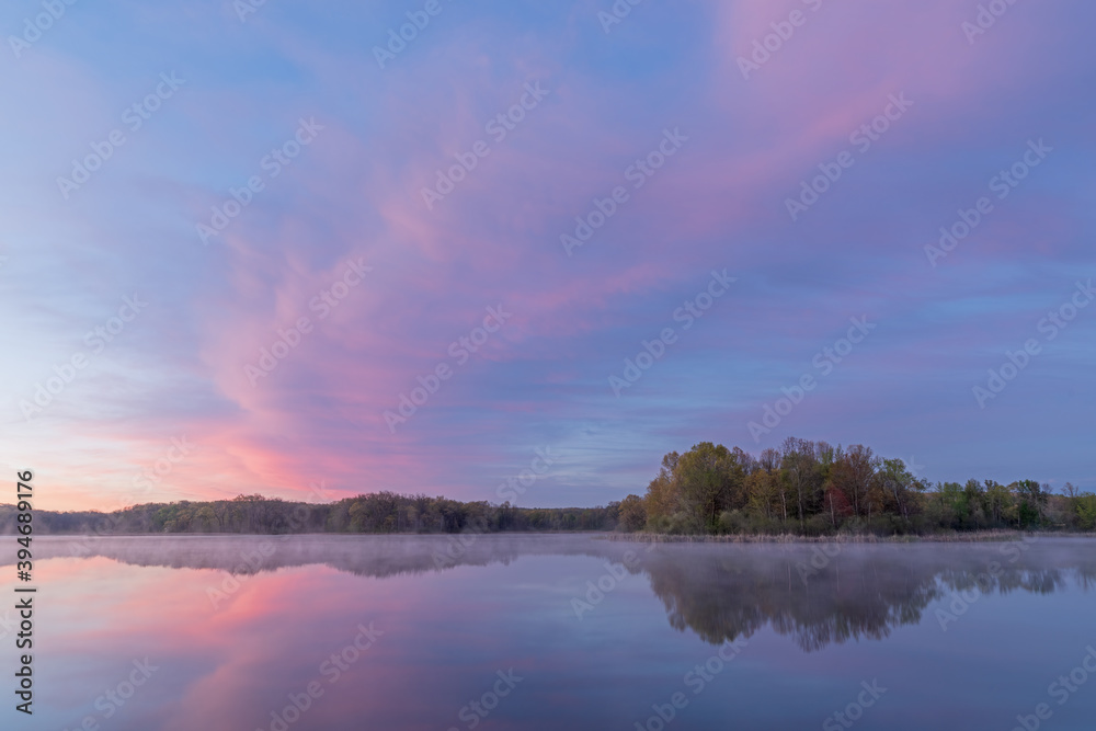 Fototapeta premium Landscape at dawn of the foggy, spring shoreline of Whitford Lake with reflections in calm water, Fort Custer State Park, Michigan, USA