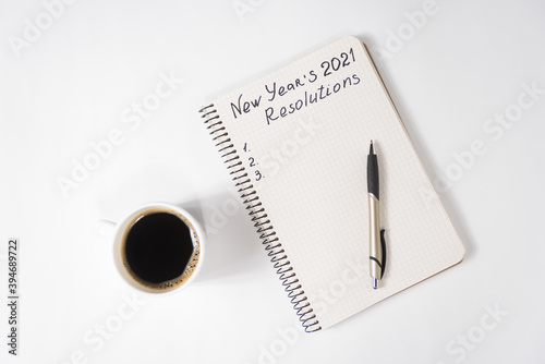 Phrase New Year s Resolutions 2021 in the notebook and pen. Cup of coffee on table