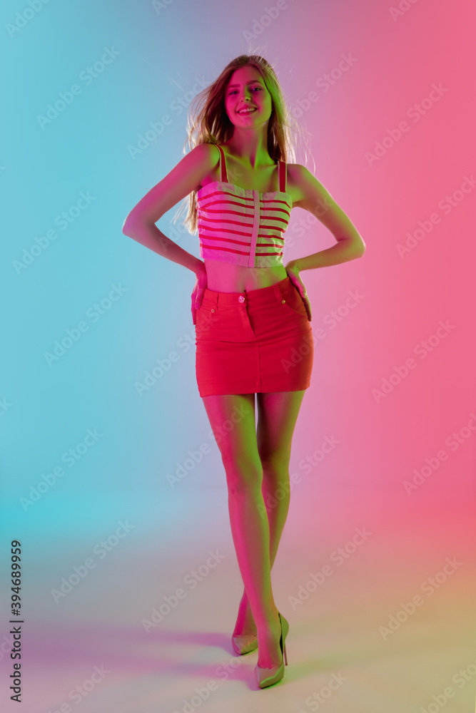 Spring. Beautiful young girl in fashionable, romantic pink outfit on gradient pink-blue background in neon light. Full-length portrait. Copyspace for ad. Summer, fashion, beauty, emotions concept.