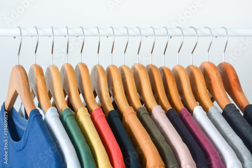 close up collection of colorful t-shirts hanging on wooden clothes hanger in closet or clothing rack over white background