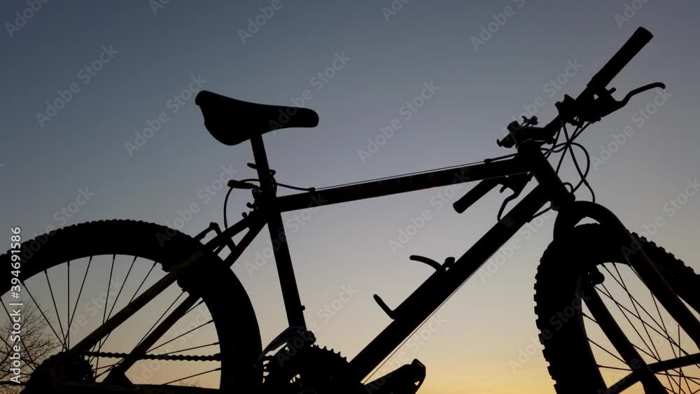 Silhouette of a bicyclist on a background of a golden sky before sunrise or after sunset. The teenager rides a bicycle along the embankment. Sports lifestyle. Silhouette of a bicyclist on a background of a golden sky before sunrise or after sunset. The teenager rides a bicycle along the embankment. Sports lifestyle.