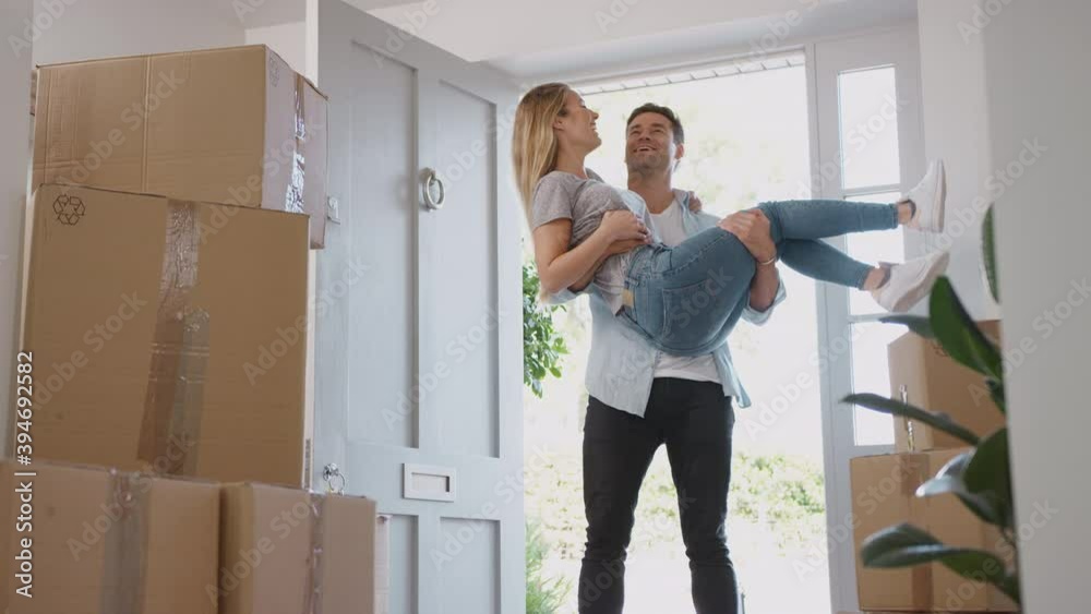 Man carrying woman over threshold and she kisses him as couple move into new home on moving day - shot in slow motion