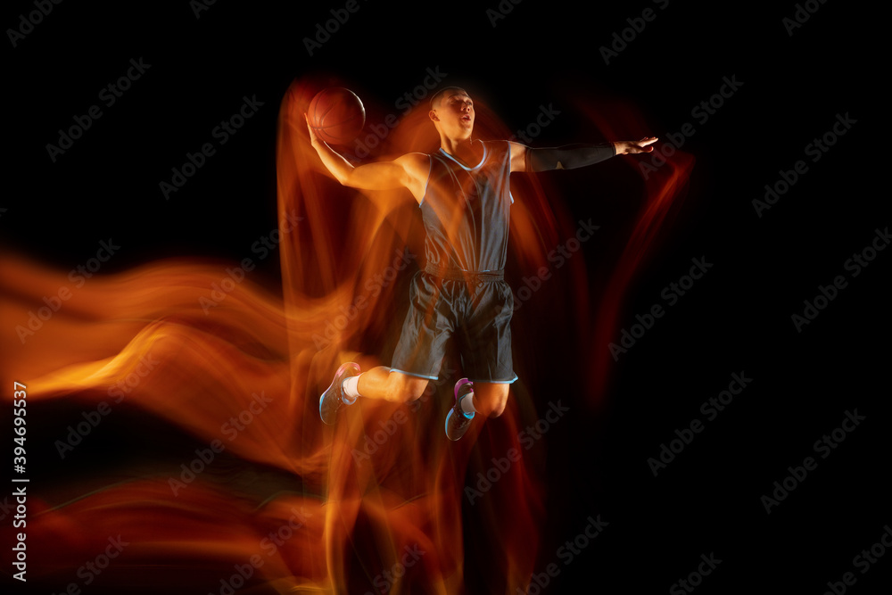 The fire tracks. Young east asian basketball player in action and motion jumping in mixed light over dark studio background. Concept of sport, movement, energy and dynamic, healthy lifestyle.