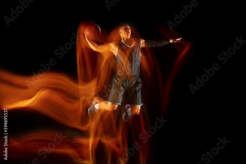 The fire tracks. Young east asian basketball player in action and motion jumping in mixed light over dark studio background. Concept of sport, movement, energy and dynamic, healthy lifestyle.