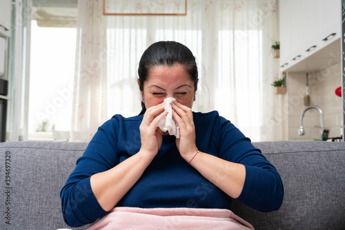 Ill adult woman blowing nose feeling unwell with cold symptoms