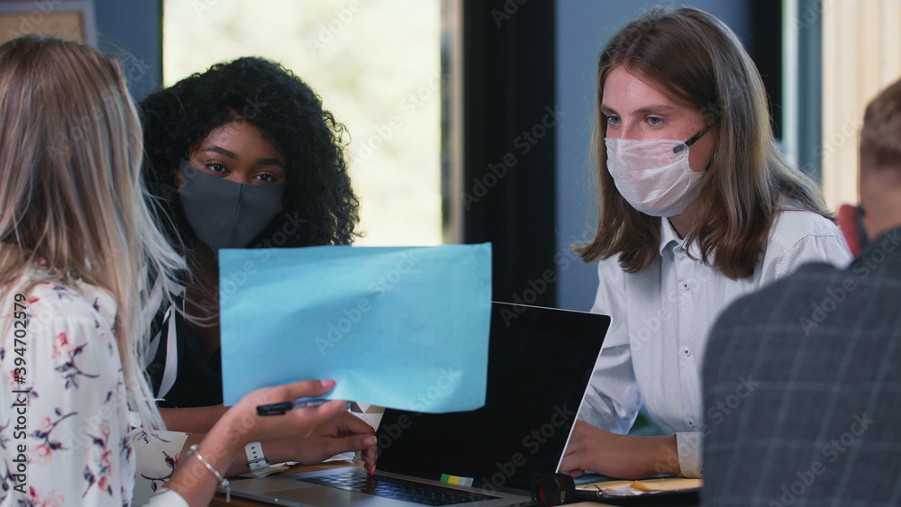 Women at workplace with COVID-19 epidemic protection. Three happy multiethnic young female colleagues work in face masks Women at workplace with COVID-19 epidemic protection. Three happy multiethnic young female colleagues work in face masks