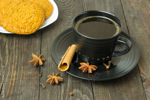 A cup of coffee, cinnamon, star anise, cloves and cookies on the table. Composition with coffee.