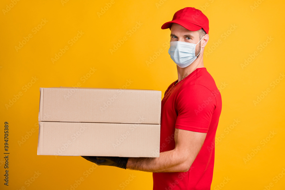 Profile photo of delivery man hold two big packages wear mask red t-shirt cap isolated yellow color background Profile photo of delivery man hold two big packages wear mask red t-shirt cap isolated yellow color background