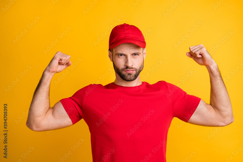 Photo of serious fit guy raise hands fists show biceps wear red t-shirt hat isolated yellow color background Photo of serious fit guy raise hands fists show biceps wear red t-shirt hat isolated yellow color background