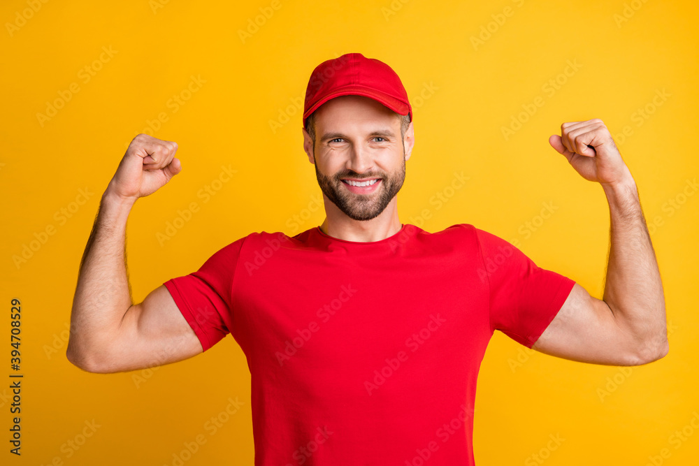 Photo of strong guy raise arms show muscles wear red t-shirt headwear isolated yellow color background Photo of strong guy raise arms show muscles wear red t-shirt headwear isolated yellow color background