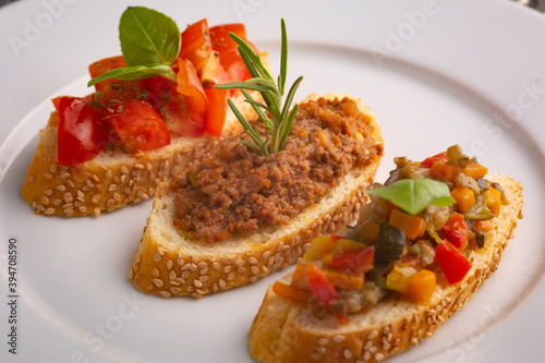 Crostini with meat sauce, tomatoes, basil and peppers on a white plate