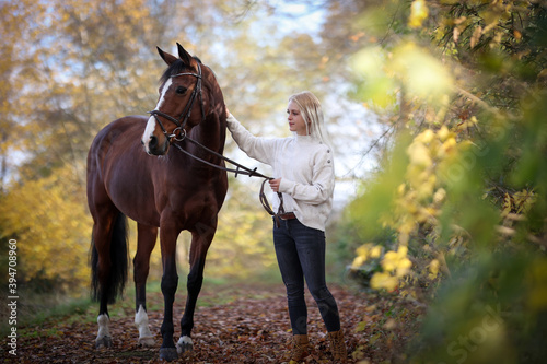 Young woman stands with her horse on a forest path in autumn.. © RD-Fotografie