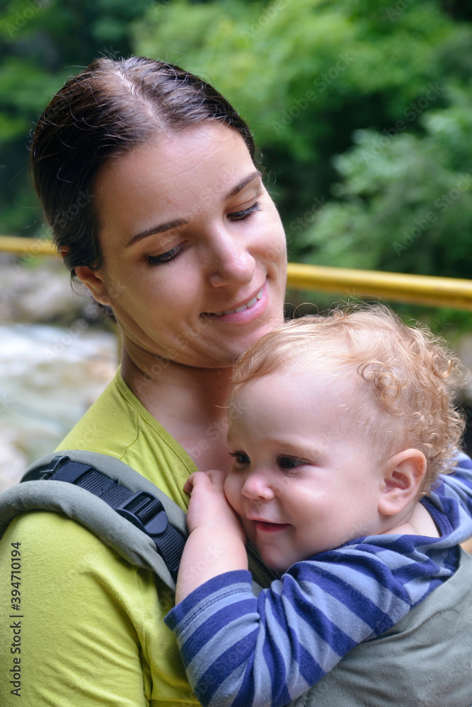 Travel with small children. Young woman with baby in carrier outdoor.