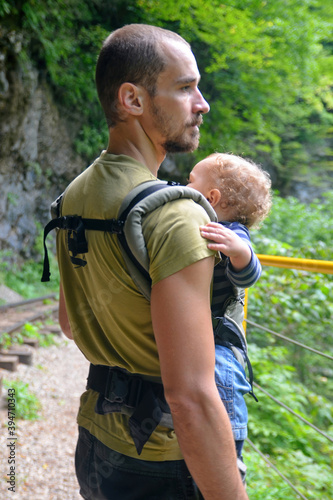 Travel with small children. Father with baby in carrier walks in mountain gorge. © Kirill