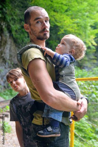 Travel with small children. Father with baby in carrier and ten year old son walking in mountain gorge. © Kirill