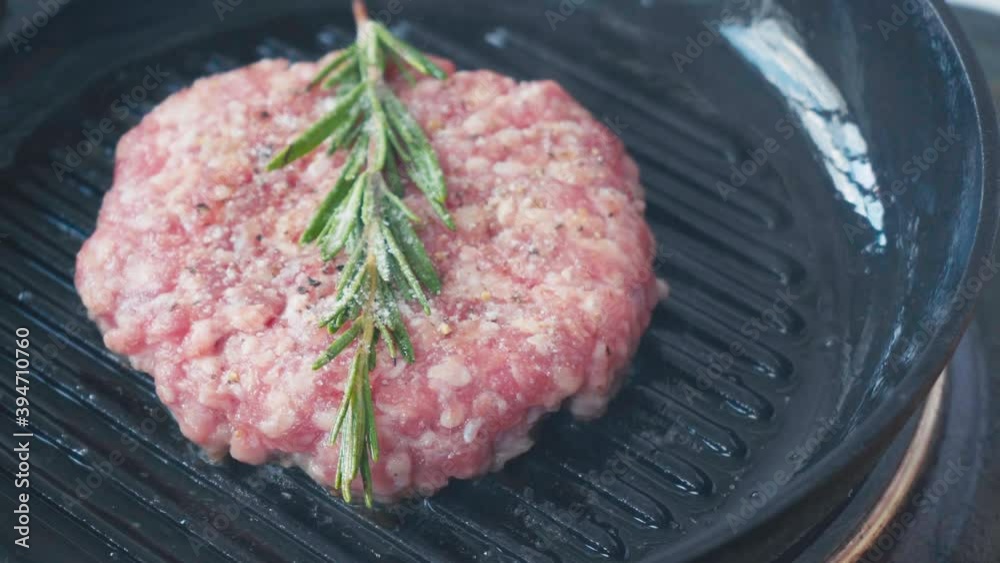 Close up view of salt falling on mince patty with rosemary branch on hot pan Close up view of salt falling on mince patty with rosemary branch on hot pan