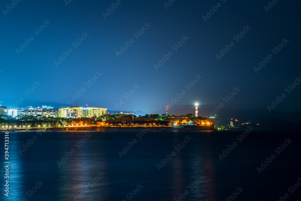 Sea night landscape with cape, illuminated buildings and lighthouse.