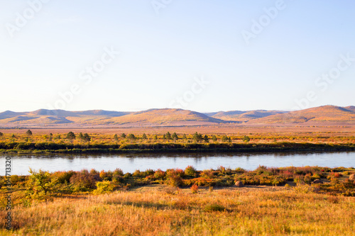  The river flows through the autumn forest. Horizontally.