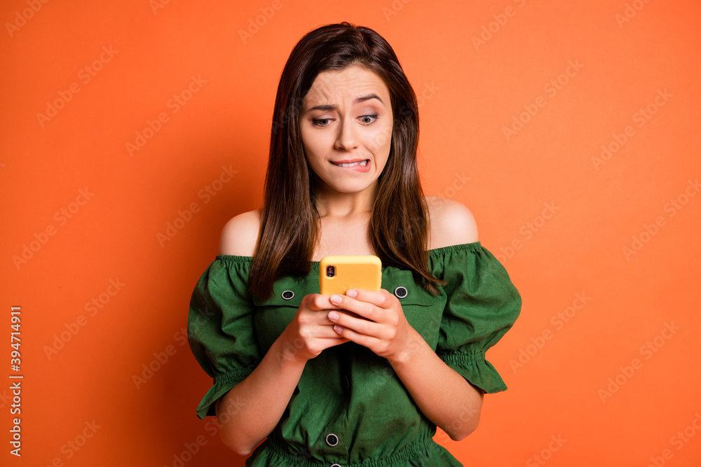 Photo of impressed woman hold telephone bite mouth wear dark shirt isolated on orange color background Photo of impressed woman hold telephone bite mouth wear dark shirt isolated on orange color background