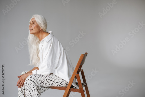 Elderly white-haired woman looking aside while sitting on chair