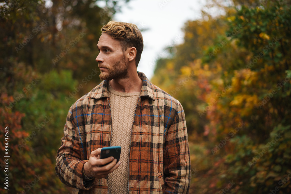 Handsome man using mobile phone while strolling in autumn forest
