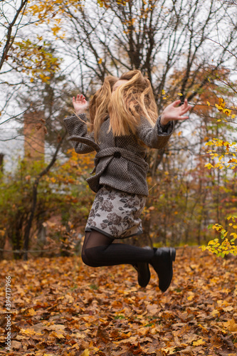 cute brunette teen girl in gray coat jumps in the autumly forest . Cosiness, autumn, fun