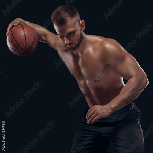 Portrait of a very muscular naked man playing basketball isolated on black background © satyrenko