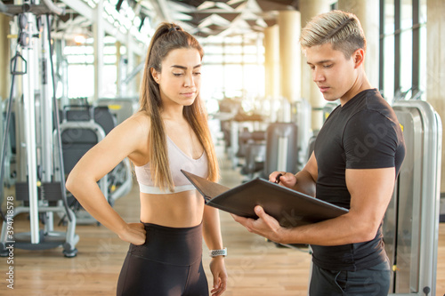 Handsome male trainer and his female client discussing her progress at the gym