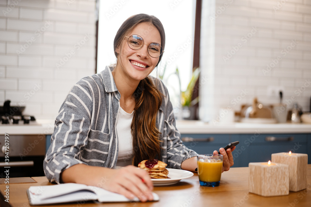 Woman writing down notes and using cellphone while having breakfast Woman writing down notes and using cellphone while having breakfast