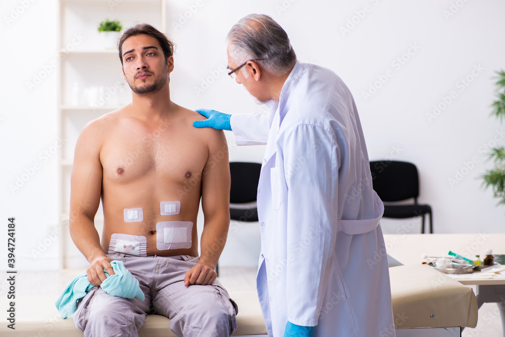 Injured young man visiting experienced male doctor Injured young man visiting experienced male doctor