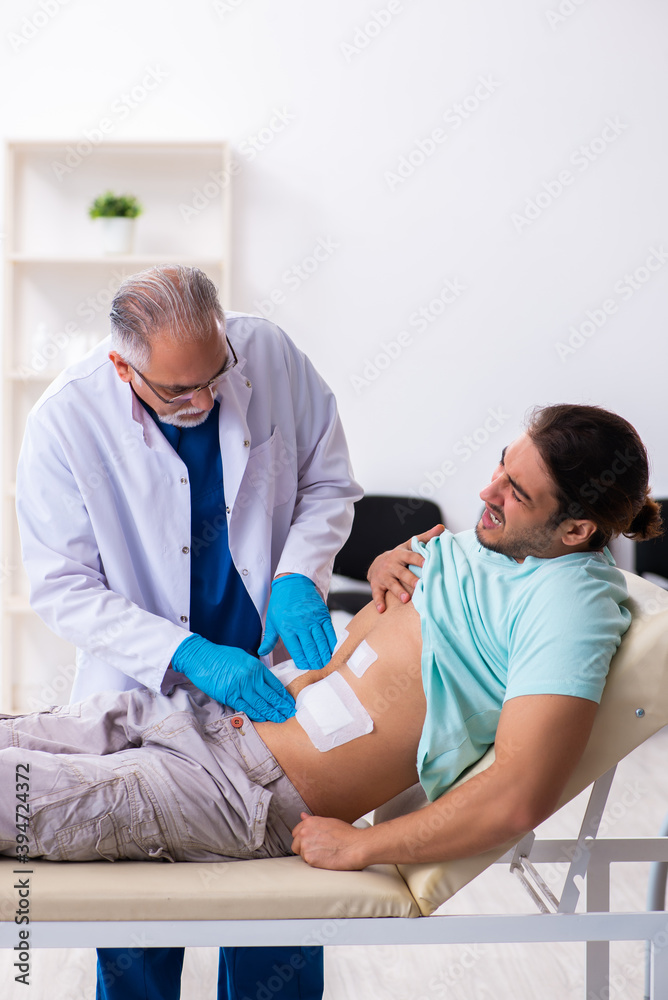 Injured young man visiting experienced male doctor Injured young man visiting experienced male doctor