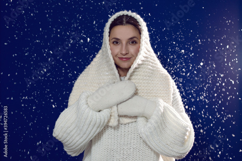 Christmas beautiful brunette girl stands in a white knitted sweater and hat at night with snow