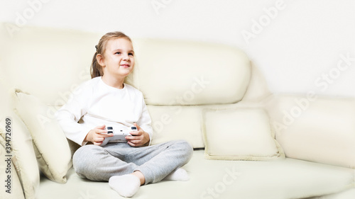 girl sits in the living room and plays video games on a console or PC with a joystick, looking at a screen or TV in the white light of an interior room at home. Lifestyle. playing online video games 
