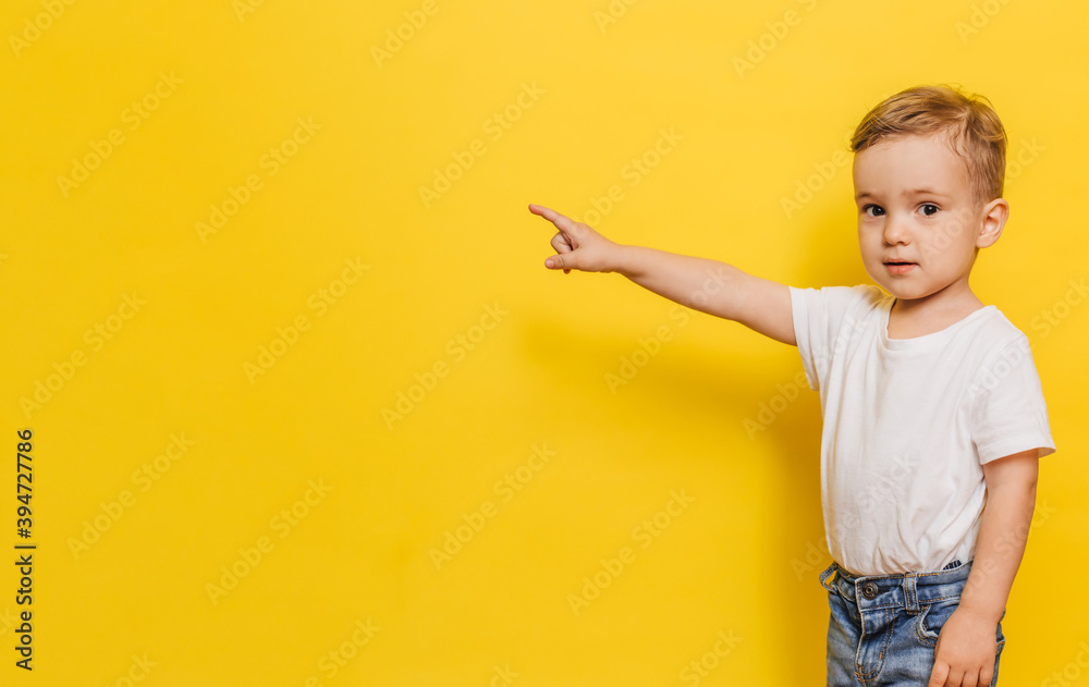A little boy on a yellow background points to the background. Copy space. A little boy on a yellow background points to the background. Copy space.