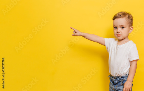 A little boy on a yellow background points to the background. Copy space.