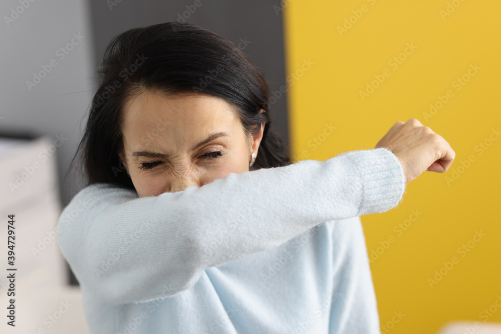 Young Woman sneezes into her elbow. Virus spreading through sneezing concept Young Woman sneezes into her elbow. Virus spreading through sneezing concept