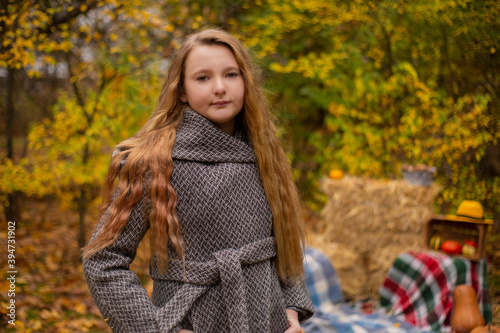 cute brunette teen girl in gray coat near autumn elements decoration - pumpkins, apples, plaid, hay. Cosiness, autumn