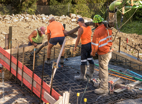 Tradesmen using concrete pump to pour footings on building site