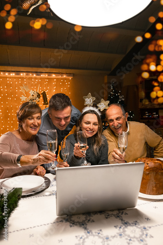 Fotografie Happy family greeting their family and friends with a champagne glass, on New Year's eve using a skype video call