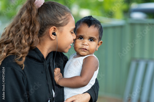 Teen girl with earbuds in ears holding and cuddling baby photo