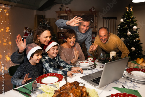 Happy and Excited family greeting their family and friends on Christmas eve using a skype video call during the coronavirus pandemic. Some relatives waving and talking to a laptop. Social distancing.