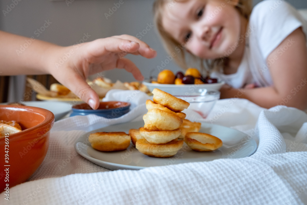 Delicious breakfast with tiny mini pancakes, cherries, apricots, jam on a white table. Small children hold pancakes in their hands. view from above Delicious breakfast with tiny mini pancakes, cherries, apricots, jam on a white table. Small children hold pancakes in their hands. view from above